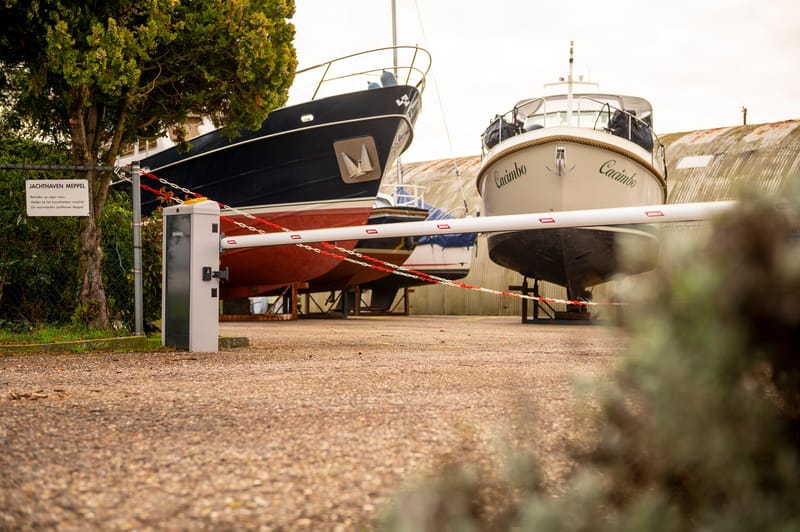 Slagboom bij de ingang van een jachthaven, met boten op de wal